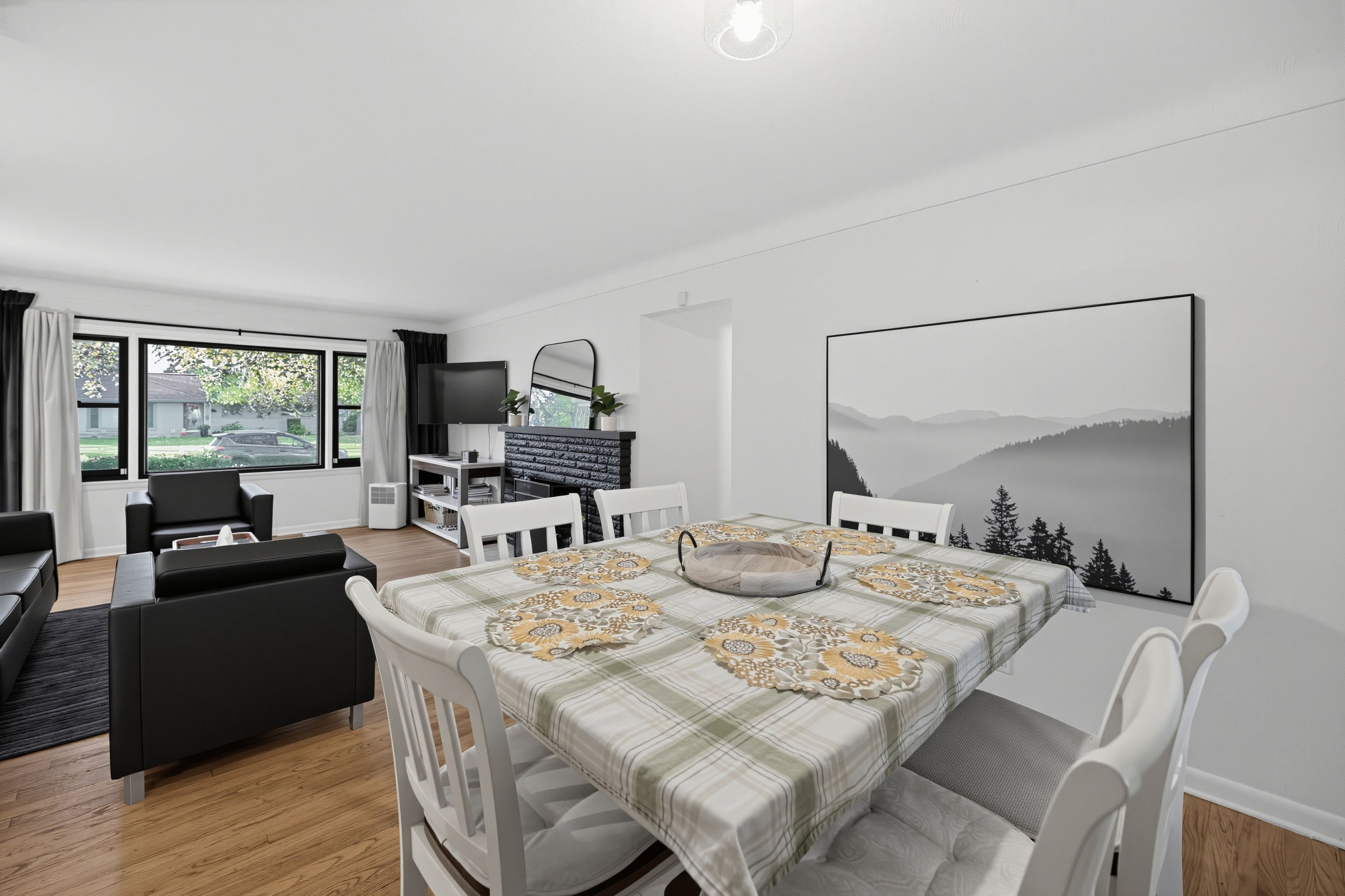 A modern living room with a dining area, a flat-screen TV, and a large landscape painting.