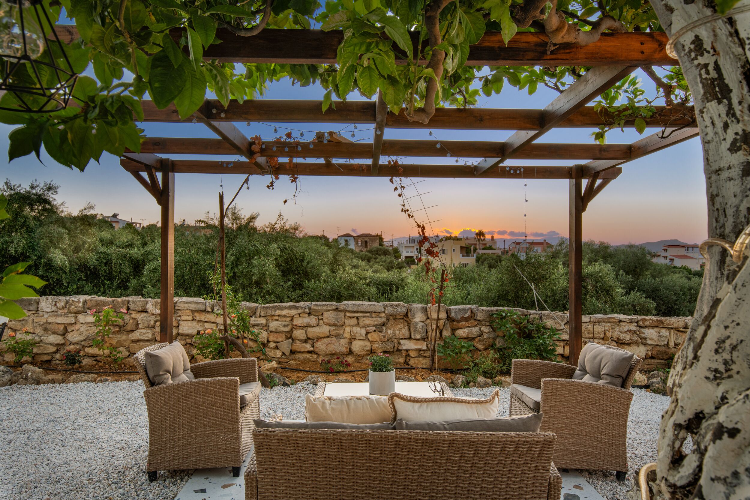 A covered outdoor seating area with wicker furniture and a stone wall backdrop.