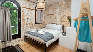 A bedroom with a stone wall, a bed with white linens, a hanging light fixture, and a wooden easel with a blue garment. - Beit Petra Chania (Chania)