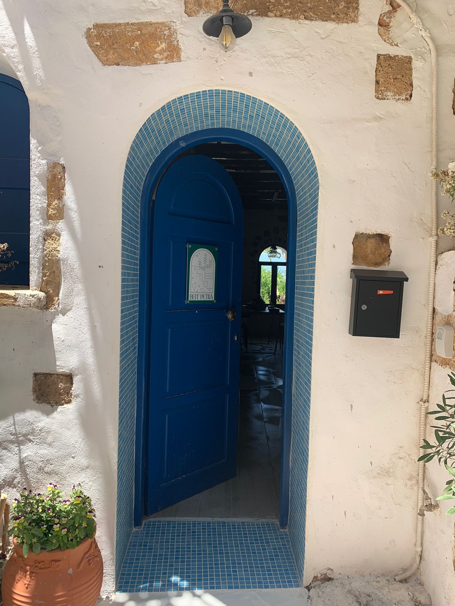 A blue door with a sign reading "BETT PETRA" leading into a room with a tiled floor and a small potted plant.