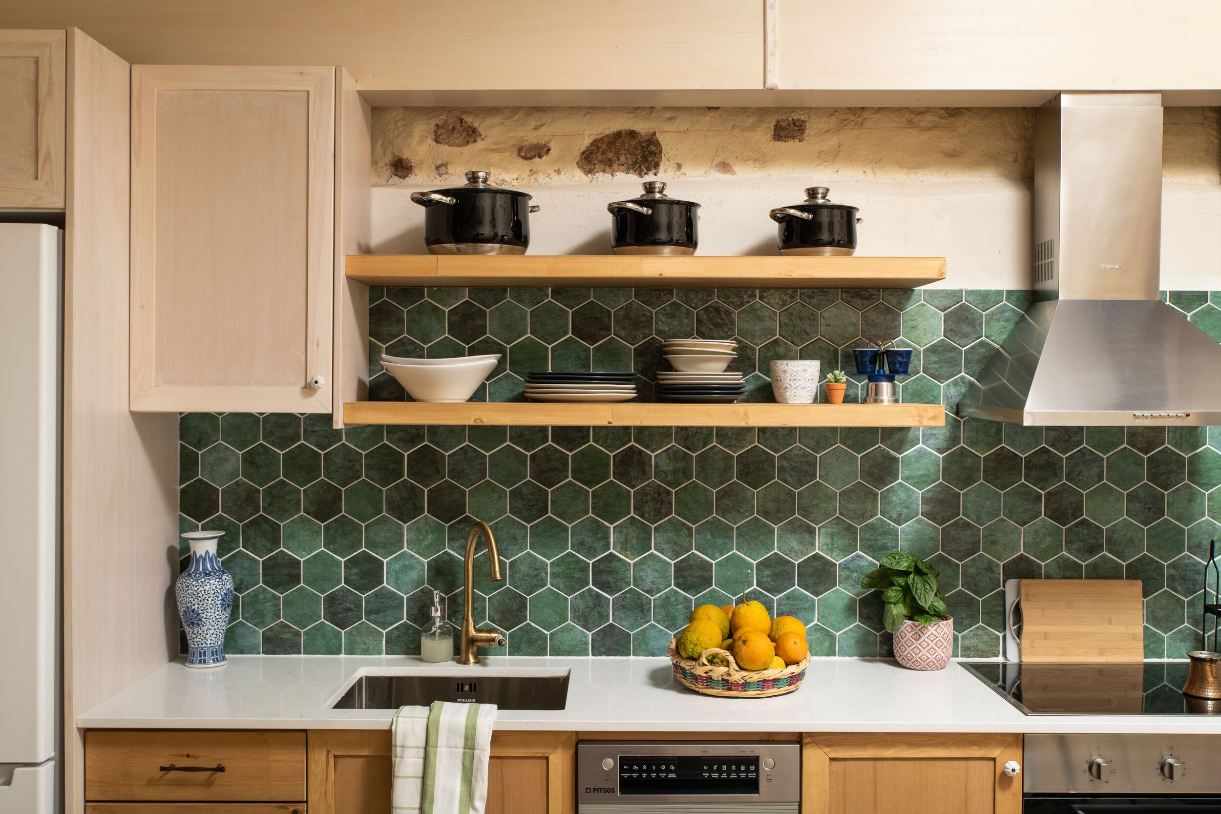A kitchen with wooden cabinets, a white countertop, a green-tiled backsplash, and a stainless steel range hood.