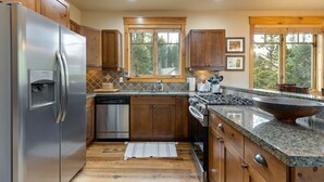 A modern kitchen with wooden cabinets, stainless steel appliances, granite countertops, and a large window providing natural light. - 6554 Settlers Creek 3 Bedroom Townhouse by RedAwning (Keystone)