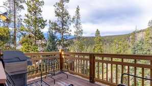 A wooden deck with a grill and chairs, overlooking a forested area with mountains in the background. - 6554 Settlers Creek 3 Bedroom Townhouse by RedAwning (Keystone)
