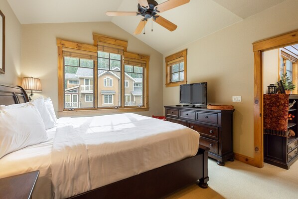 Un dormitorio con cama, televisión, ventanas de madera y ventilador de techo.