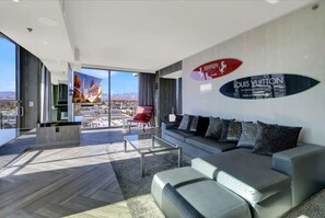 Een moderne woonkamer met een grote bank, een salontafel en een rode fauteuil. Twee grote ramen bieden uitzicht op de stad.