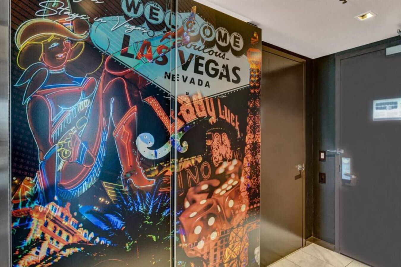 A glass partition with neon signs and artwork depicting Las Vegas landmarks.
