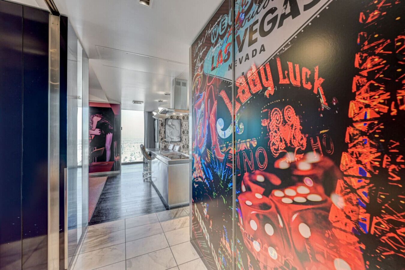 A hotel corridor with a view of a bar area, a poster with 'Los Vegas' and 'Baby Luck' text, and a glimpse of a room with a bed and a window.