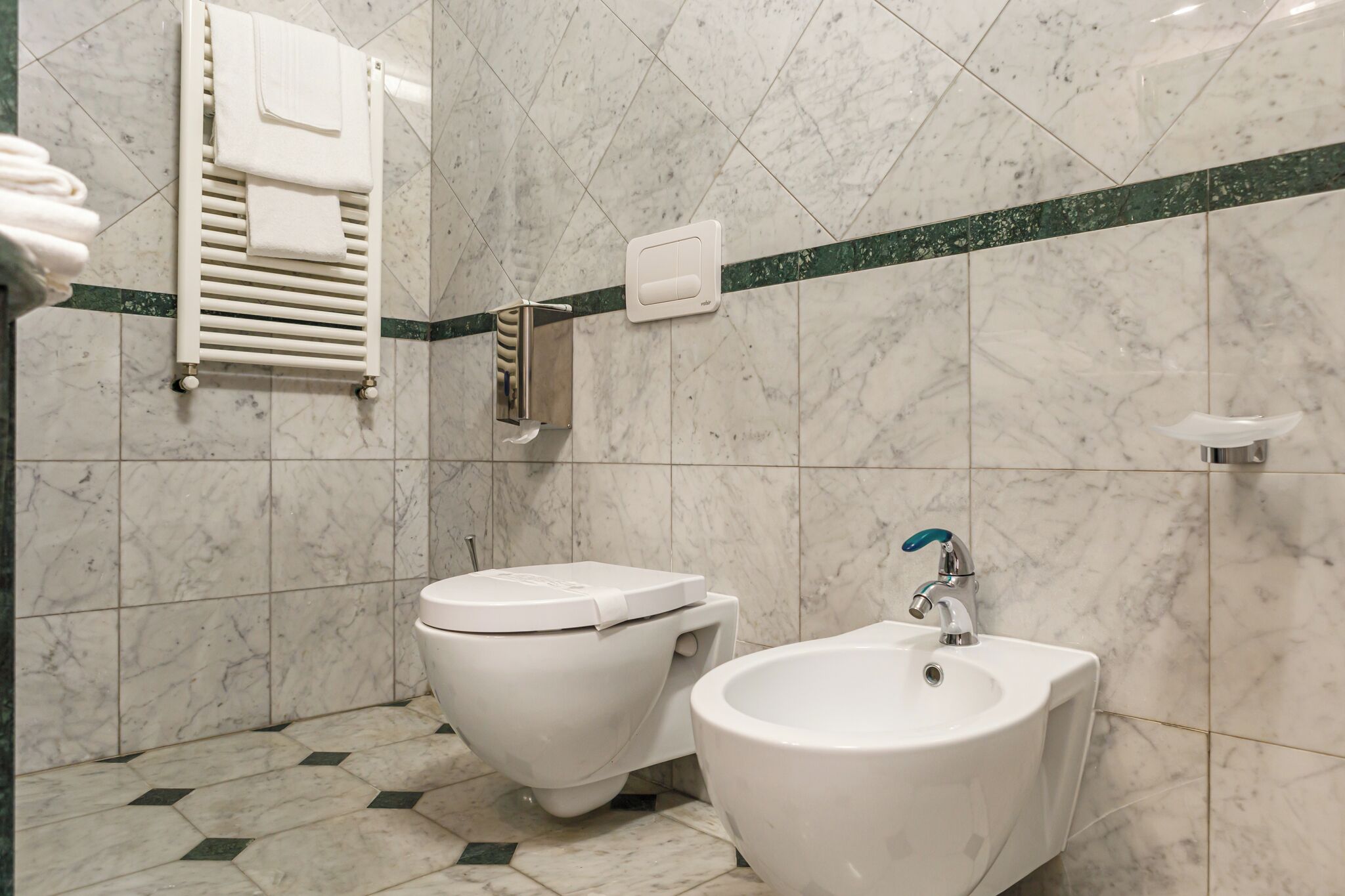 Un baño con inodoro, bidé y toallero.