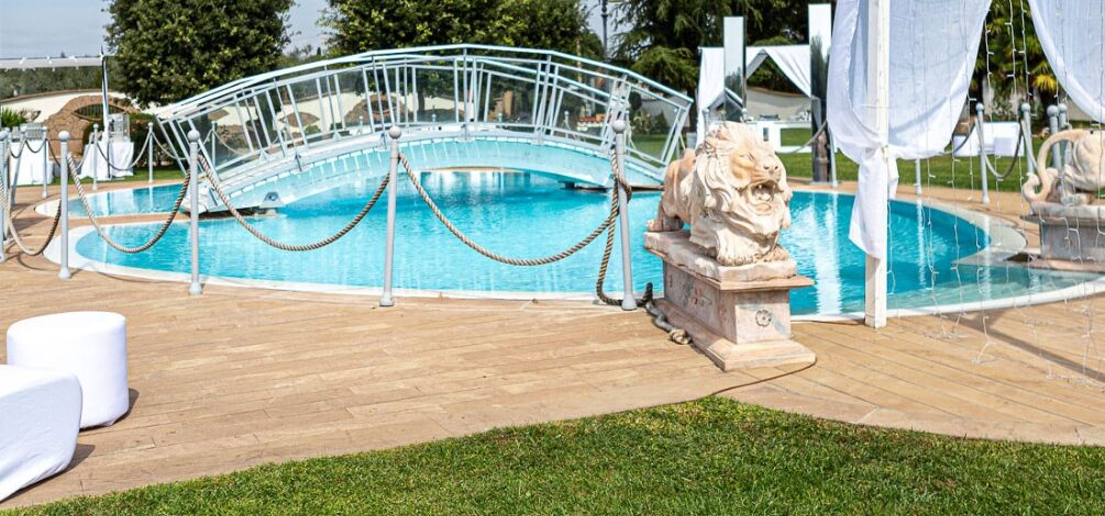 A pool area with a white bridge, a stone lion statue, and a wooden deck.