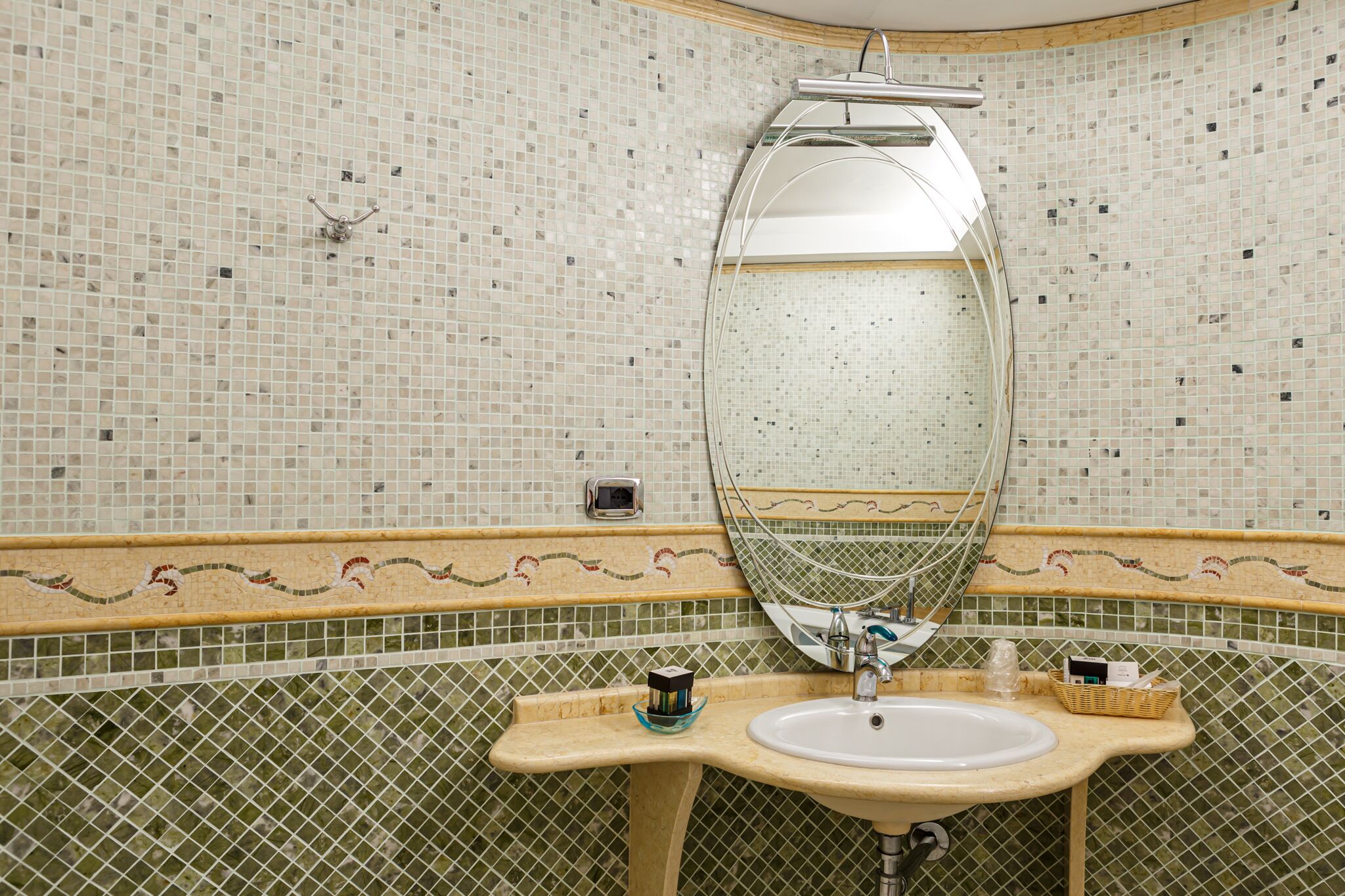 Un baño con pared de azulejos, un lavabo, un espejo y un perchero para toallas.