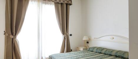 A bedroom with a bed, curtains, a nightstand, and a lamp.