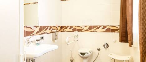 Une salle de bain avec un lavabo, des toilettes et un bidet blancs, un miroir et un espace douche.