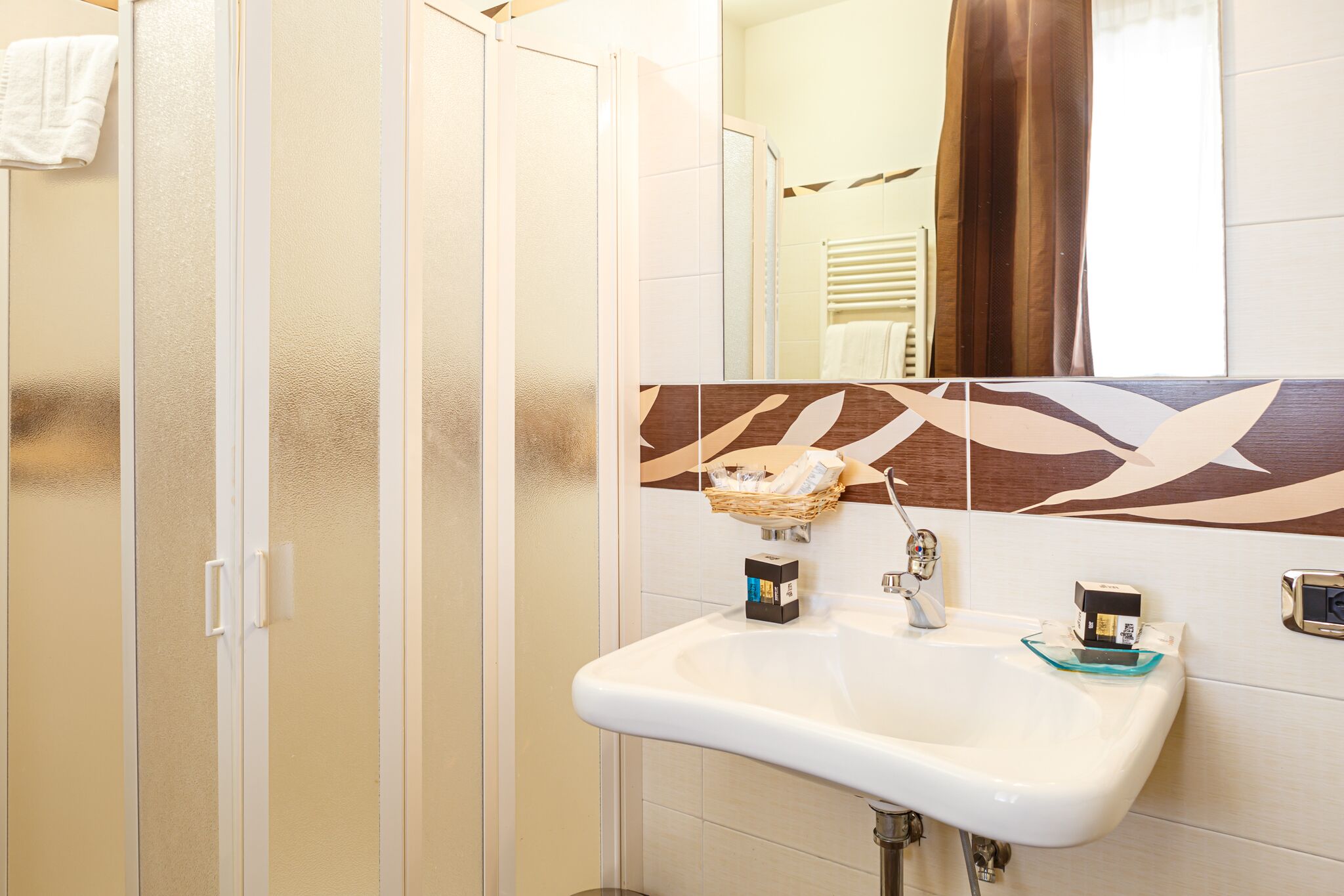 Une salle de bain dotée d’une douche à paroi de verre, d’un lavabo avec un distributeur de savon et d’un revêtement mural décoratif en carreaux.
