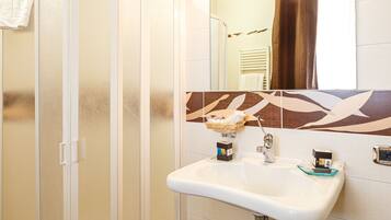 A bathroom with a glass shower enclosure, a sink with a soap dispenser, and a decorative tile backsplash.