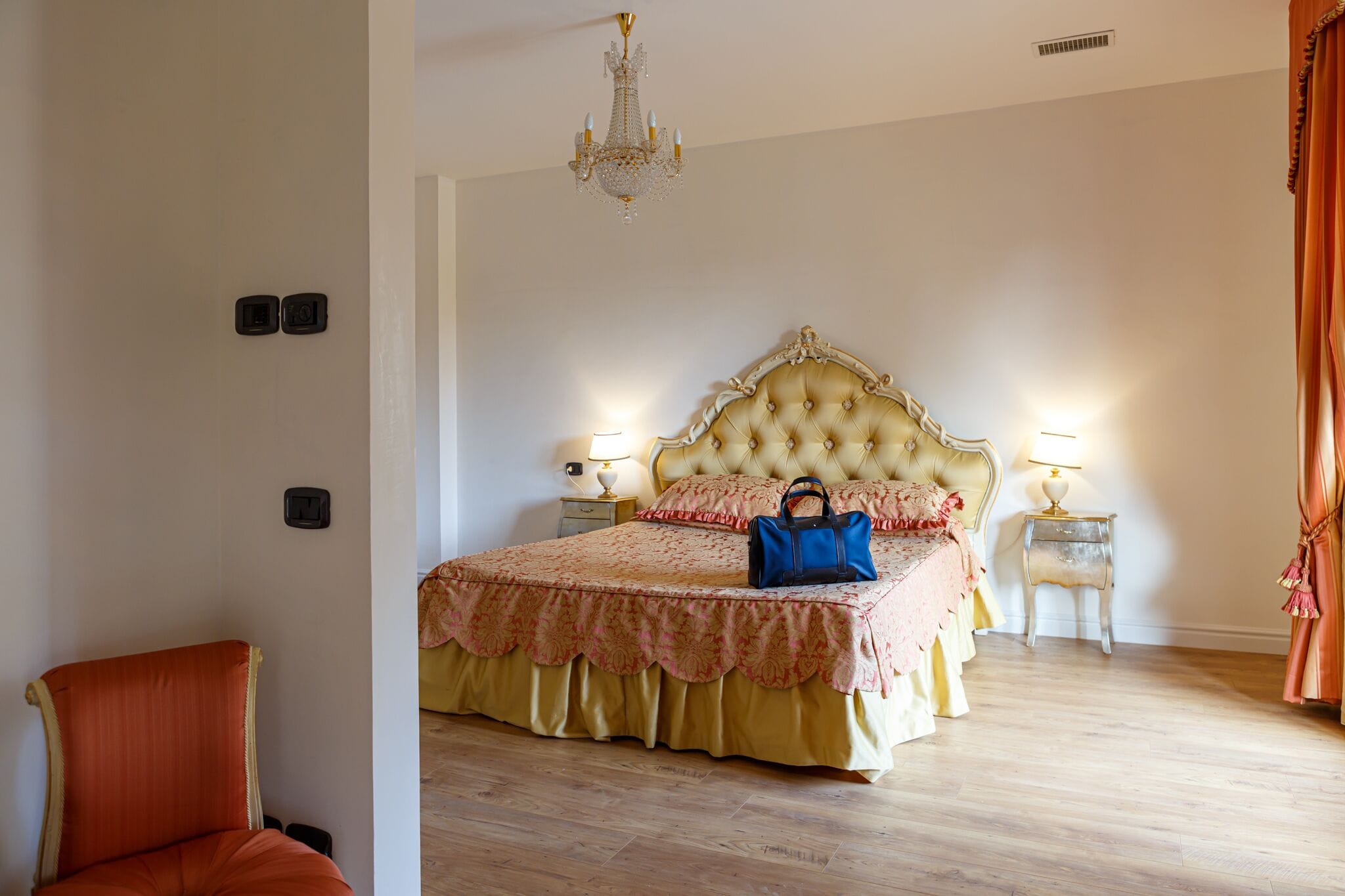 Une chambre à coucher avec un grand lit, deux tables de chevet avec des lampes, un lustre et un fauteuil.