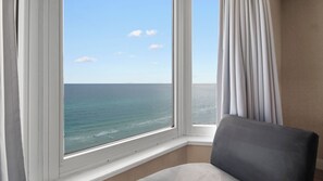 A room with a large window overlooking the ocean, a chair, and a curtain.