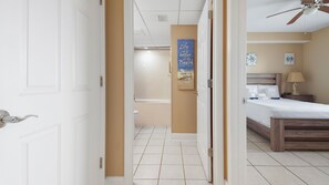 A hotel room with a bed, a nightstand, a lamp, and a bathroom visible through an open door.