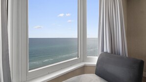 A room with a large window overlooking the ocean, a chair, and a curtain. - FREE Beach Service, Golf + Perks! Emerald Beach 1430 Pool, Hot Tub &Starbucks (Panama City Beach)