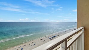 A beach view from a balcony with a railing, clear sky, and calm sea.