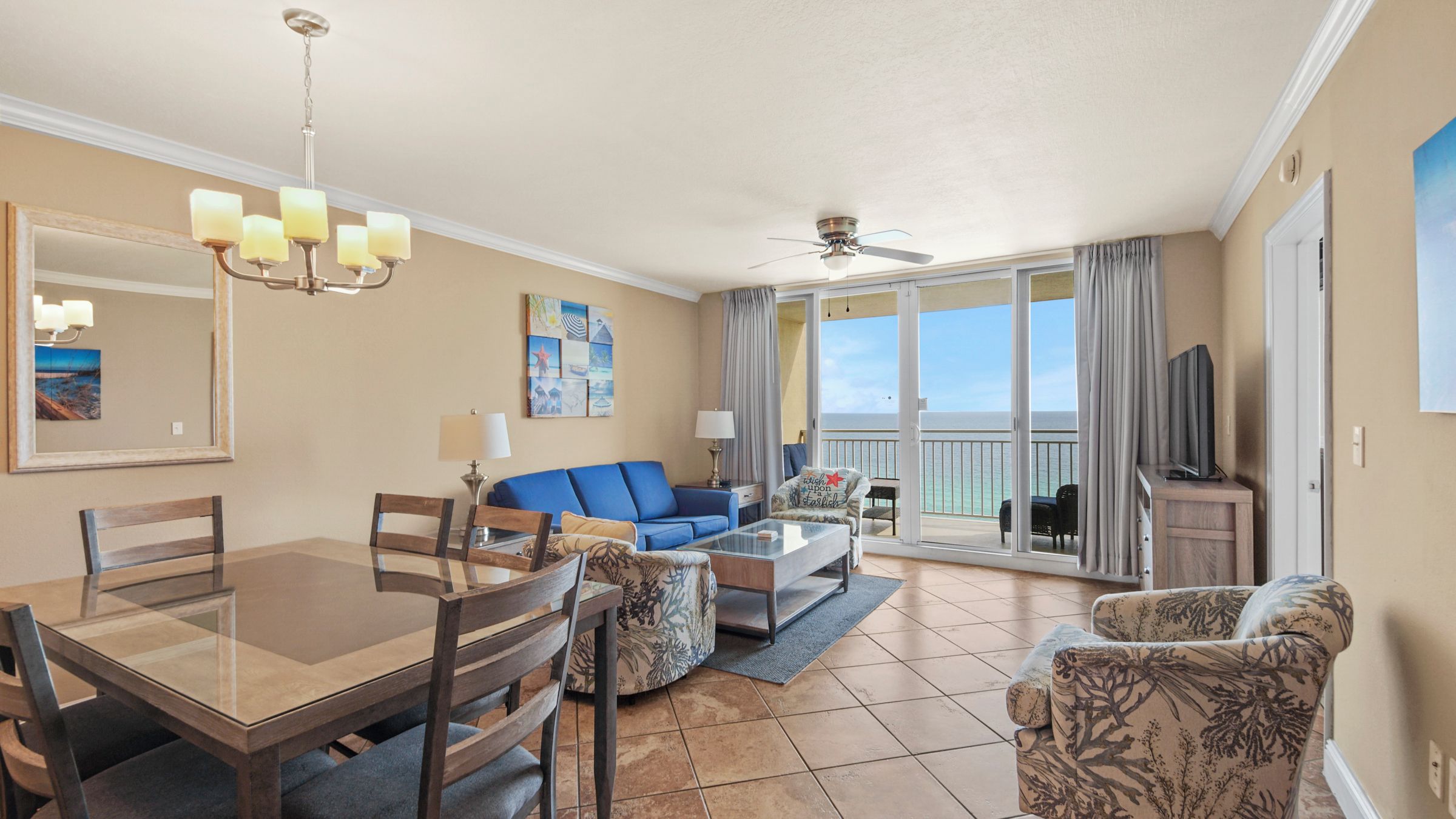 A hotel room with a dining table, chairs, a sofa, a coffee table, a TV, and a balcony with a view.
