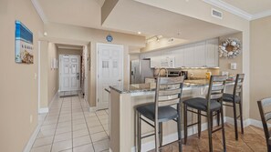 A kitchen with a central island, bar stools, and a microwave. - FREE Beach Service, Golf + Perks! Emerald Beach 1430 Pool, Hot Tub &Starbucks (Panama City Beach)