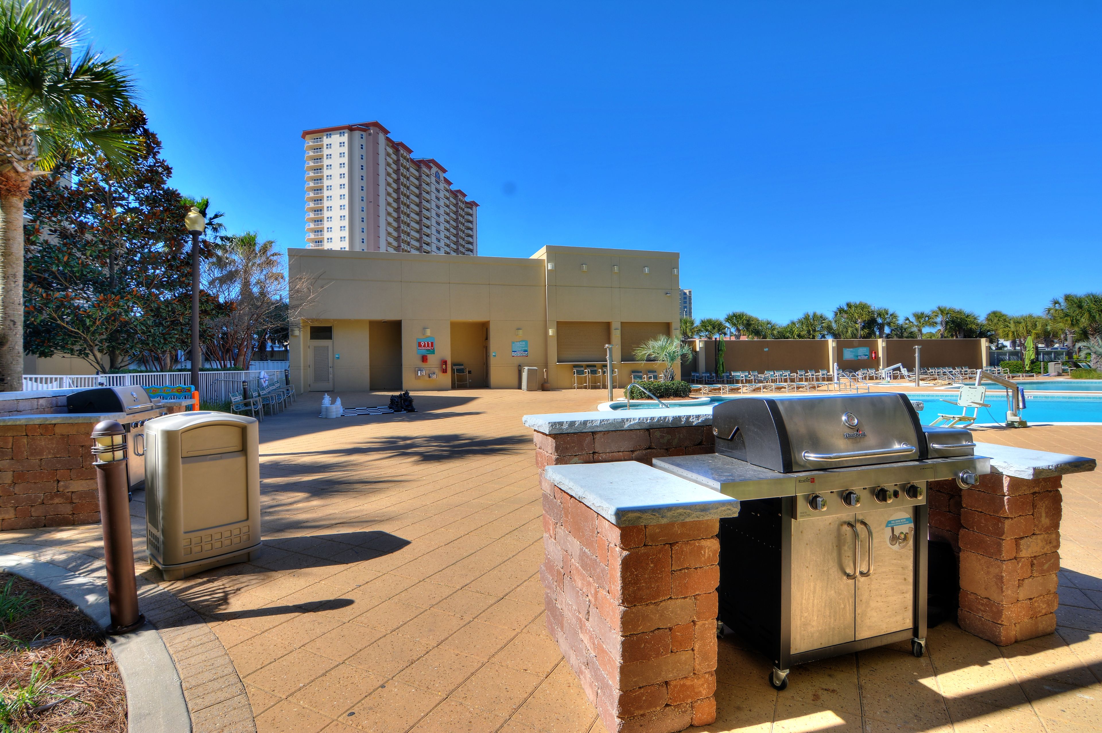 Ein Außenbereich mit Terrasse, einem Grill, einem Pool und einem mehrstöckigen Gebäude im Hintergrund.