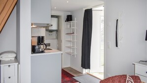 Une cuisine compacte équipée d’une machine à café, d’une étagère blanche et d’un tapis rouge à motifs.