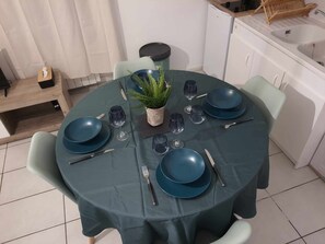 A round dining table with a dark tablecloth, surrounded by four light green chairs. - Appartement ABJ (Anneyron)