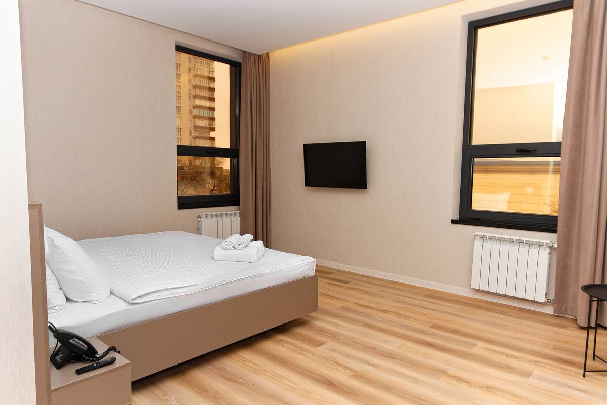 A modern hotel room with a bed, a TV mounted on the wall, and a window with curtains.