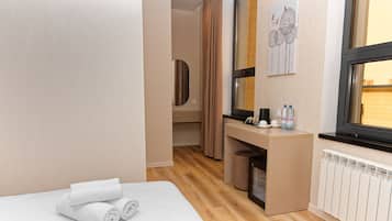 Una habitación de hotel con cama, escritorio, espejo, ventana y radiador.