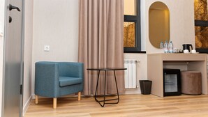A modern room with a blue armchair, a small round table, a mini fridge, a trash bin, and a large mirror. - Aston Hotel (Aktau)