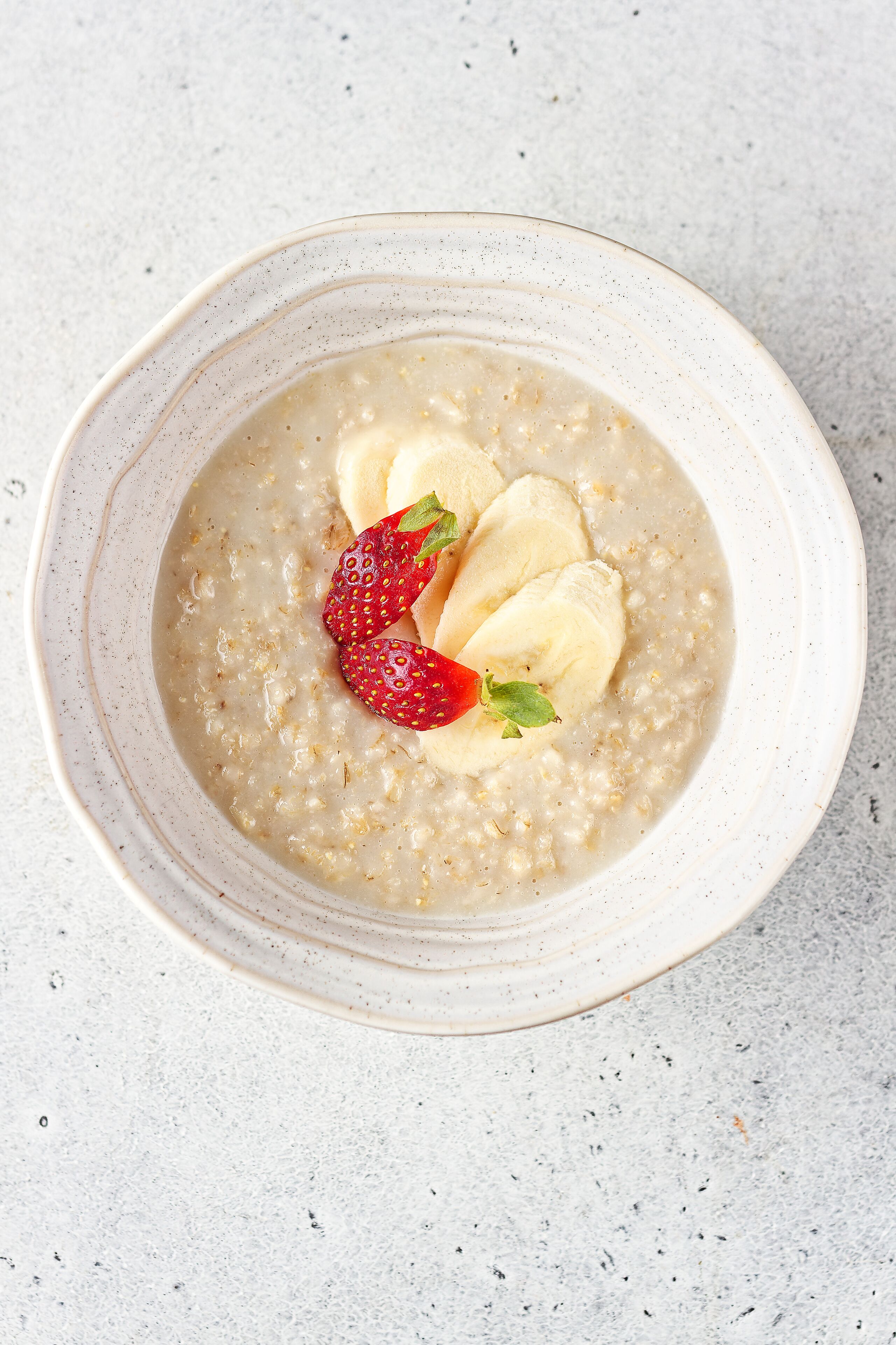 A bowl of oatmeal with sliced bananas and strawberries.