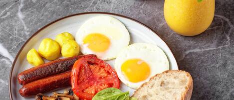 A breakfast plate with eggs, sausages, tomatoes, beans, mushrooms, spinach, and toast, along with a glass of orange juice and a vase of pink roses.