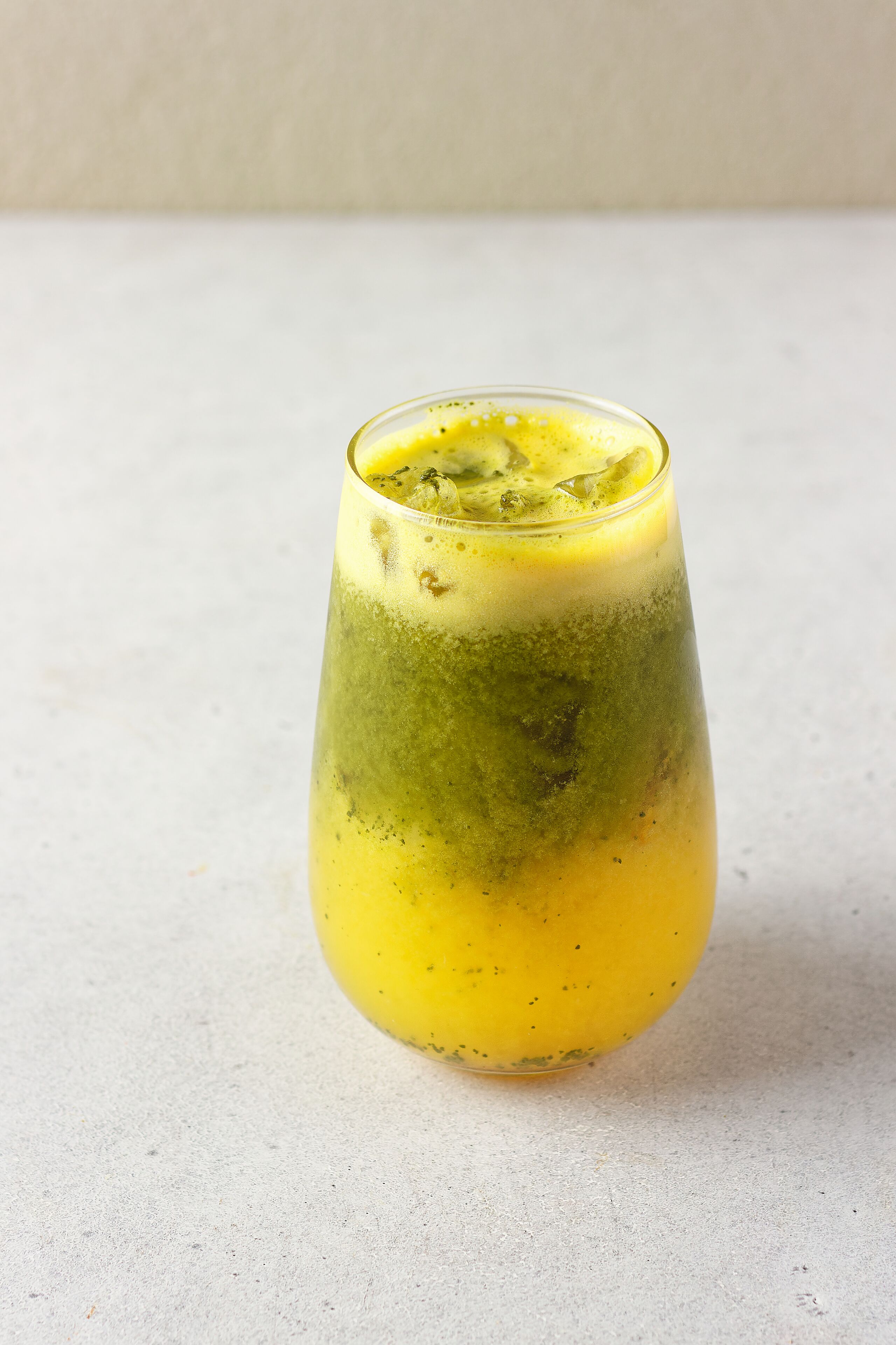 A glass of layered beverage with a gradient from yellow to green, placed on a plain surface.