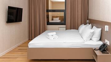 Quarto de hotel moderno com cama, televisão na parede, telefone ao lado da cama e janela com cortinas.