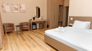 A hotel room with a bed, two armchairs, a desk with a mirror, and a small table. - Aston Hotel (Aktau)
