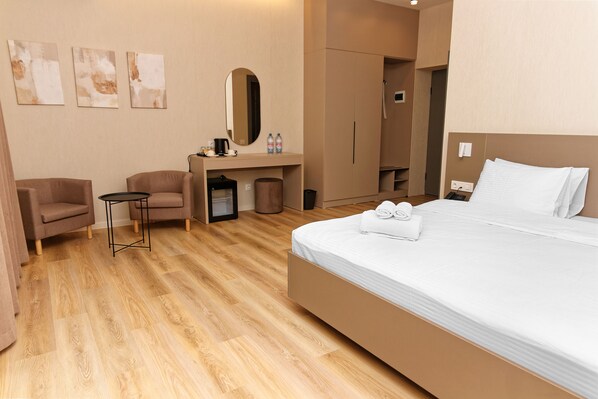 Habitación de hotel con cama, dos sillones, escritorio con espejo y una mesita.
