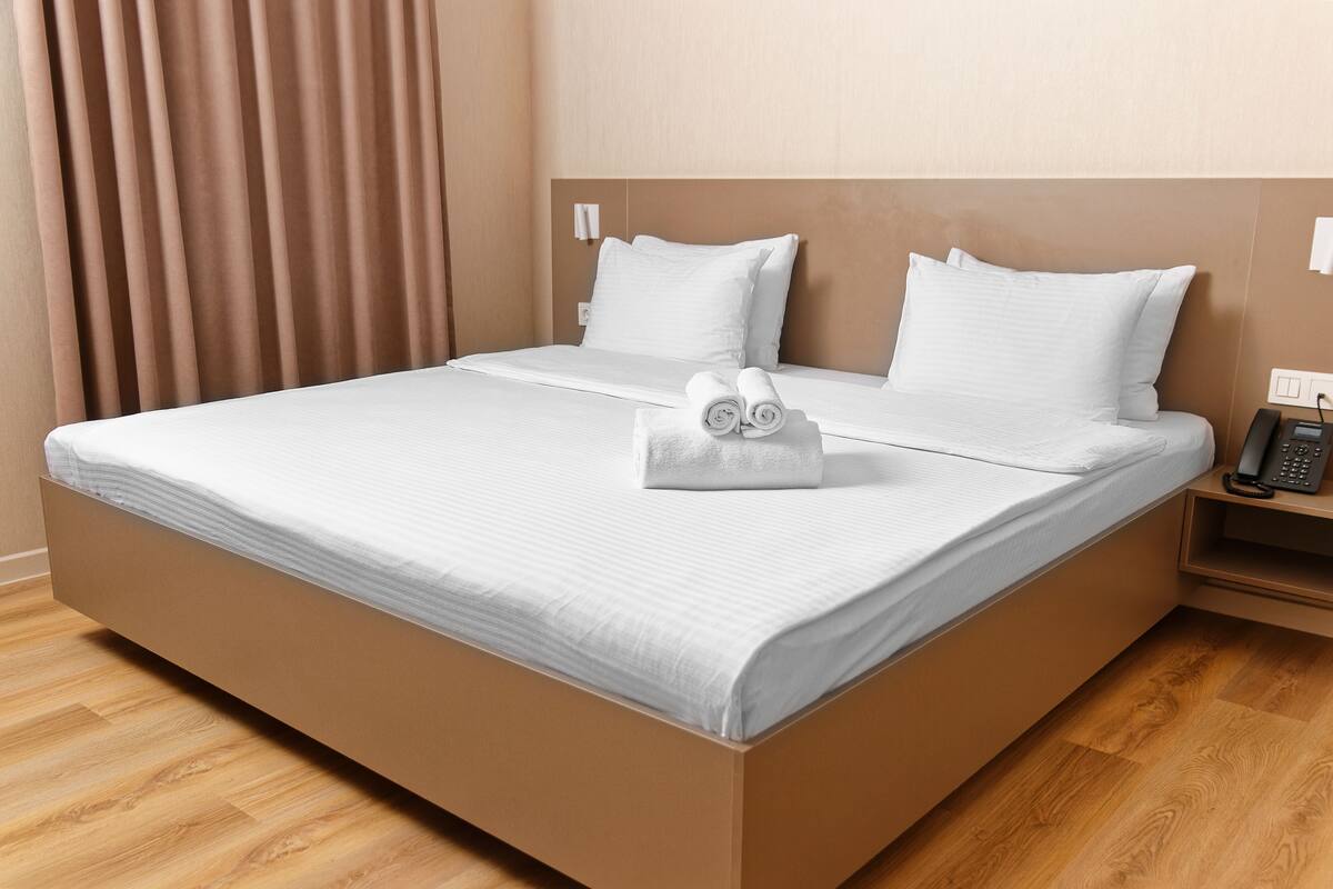 A neatly made bed with white linens, a folded towel, and a bedside phone on a wooden nightstand.