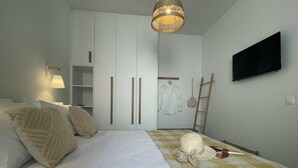 A bedroom with a bed, a wardrobe, a television, and a hanging lamp.