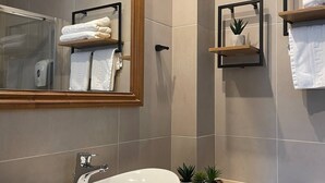 A modern bathroom with a large mirror, a white vessel sink, and two towel racks.