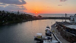 A marina with boats docked, a sunset in the background, and buildings along the waterfront.