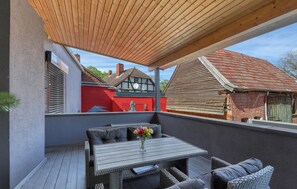 A covered outdoor seating area with a table and chairs, a wooden ceiling, and a view of traditional houses in the background. - Luxusvilla mit Kegelbahn (Bahrdorf)