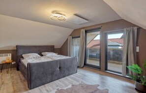 A bedroom with a large bed, a ceiling light, a window with curtains, and a view of a red-tiled roof outside. - Luxusvilla mit Kegelbahn (Bahrdorf)