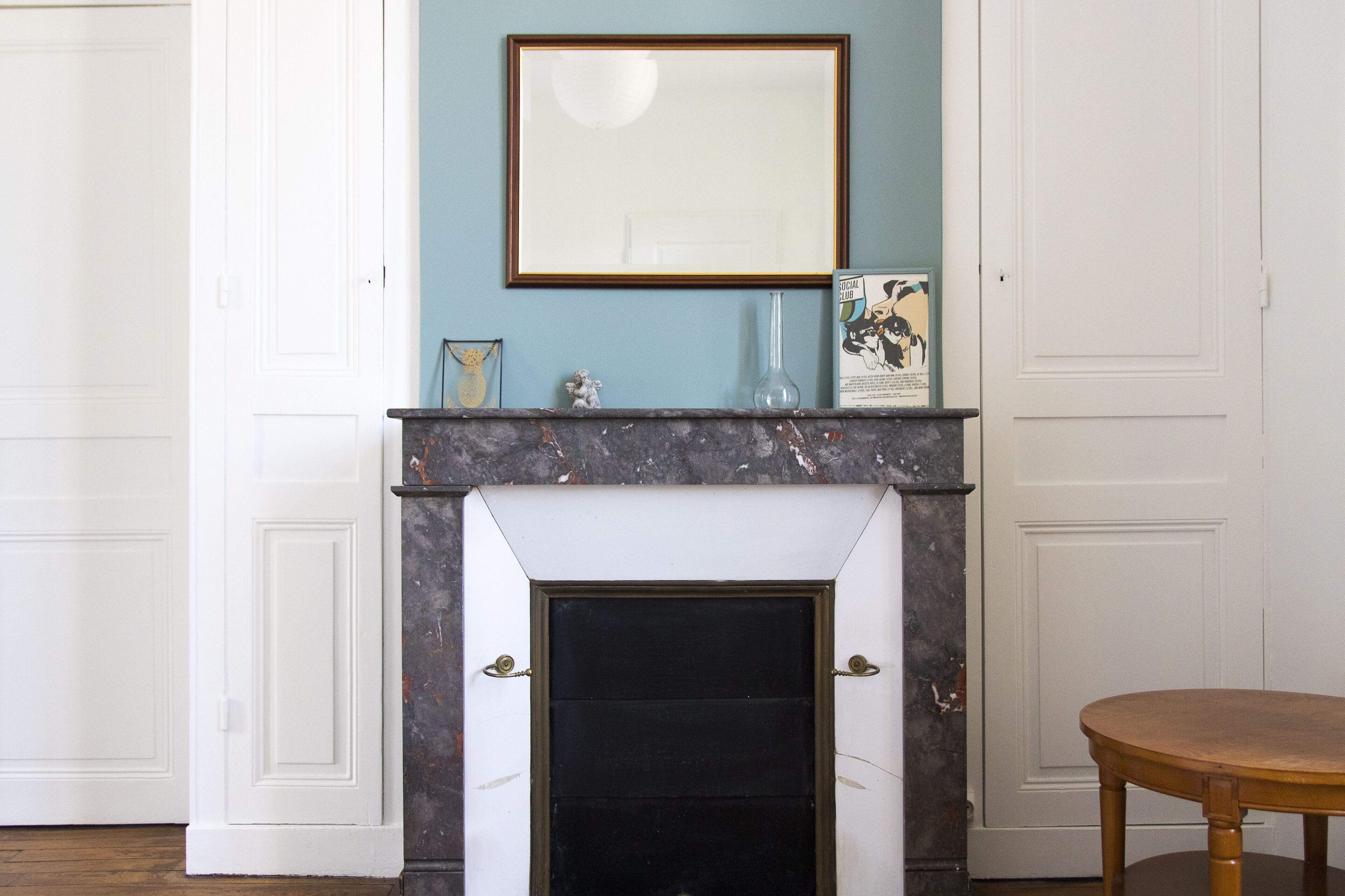 A room with a white fireplace, a framed picture above it, and a small table to the right.