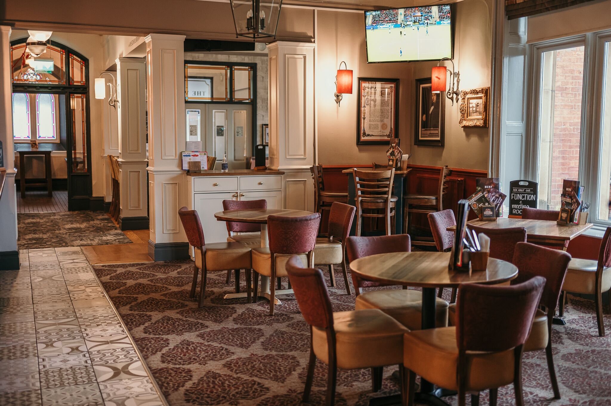 Un espace repas avec plusieurs tables et chaises, un coin cuisine doté d’un comptoir et de placards, et une grande fenêtre offrant une vue dégagée.