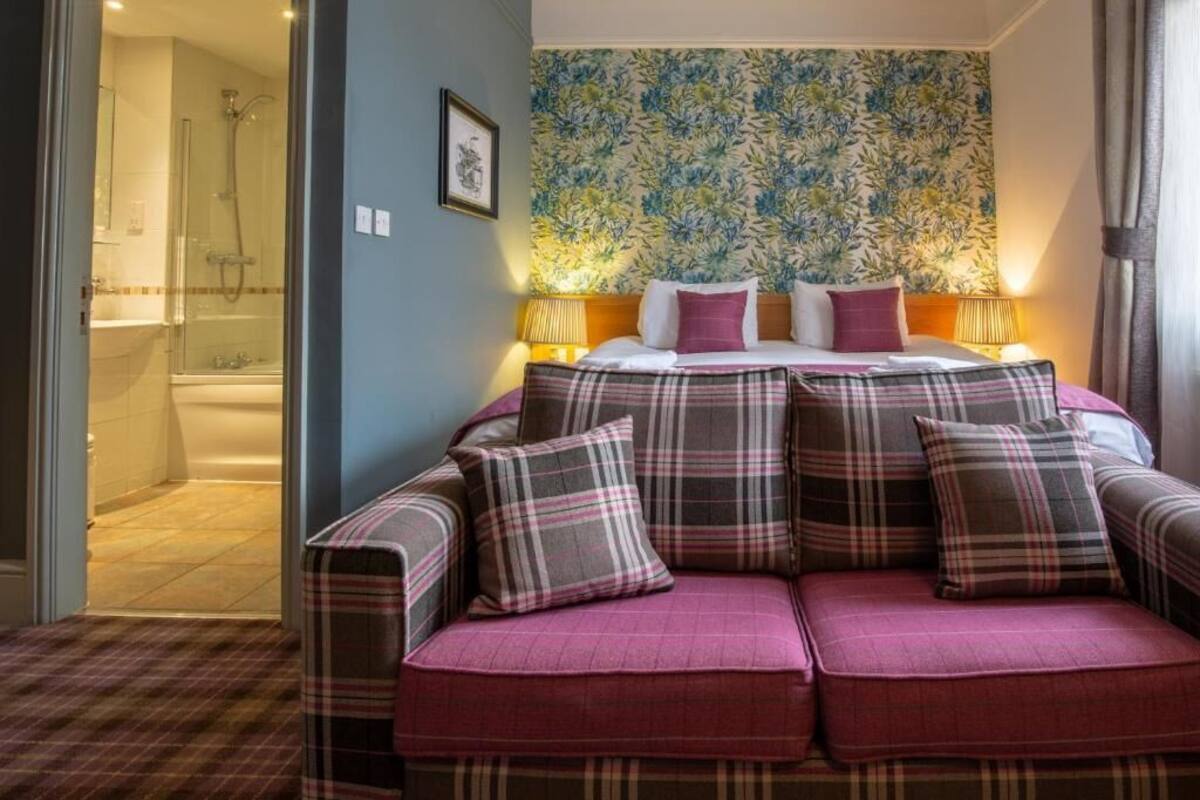 A hotel room with a bed, a sofa, a shower, and a floral wallpaper.