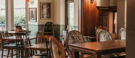 A dining area with wooden tables and chairs, patterned carpet, and a chandelier.