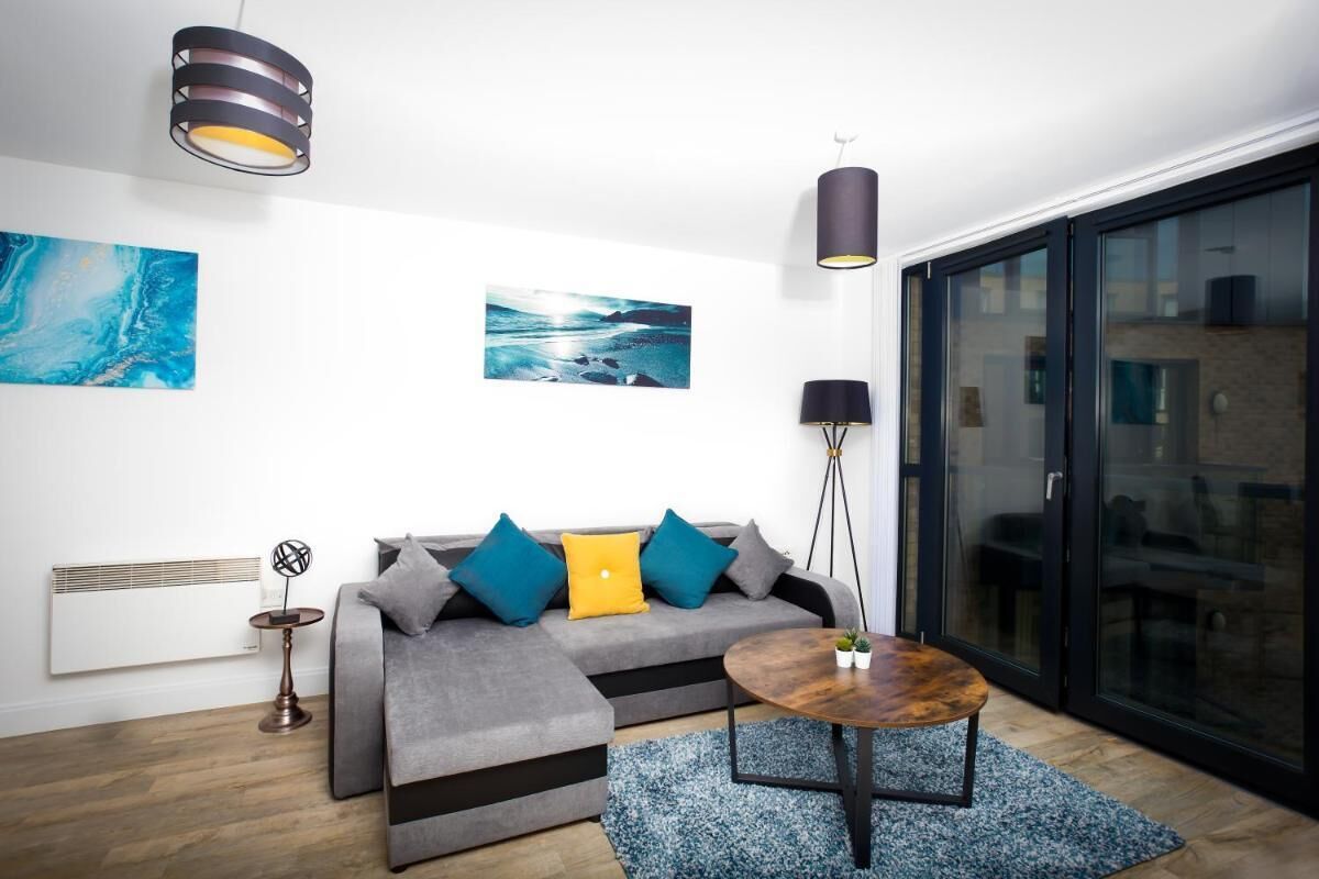 A modern living room with a grey sofa, blue and yellow cushions, a round coffee table, and a large window with a view of a building.