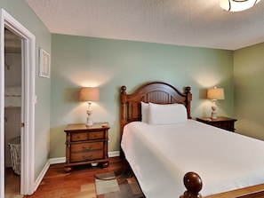 Un dormitorio con una cama de madera, dos mesitas de noche con lámparas, una mesita auxiliar de madera y un pequeño cubo de basura.