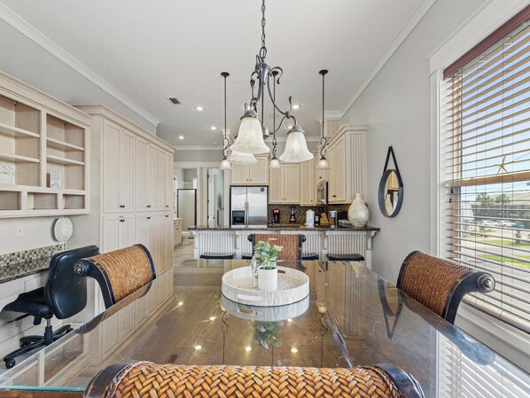 A spacious kitchen with a central island, pendant lighting, and a view of the outside through large windows.